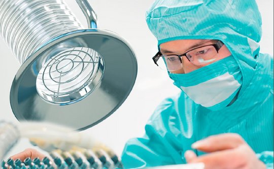 Technician in cleanroom attire working beneath a metal extraction hood