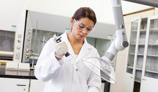 Scientist using a pipette beneath a local extraction arm in a laboratory