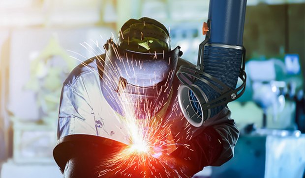 Worker welding metal while an extraction arm captures fumes nearby