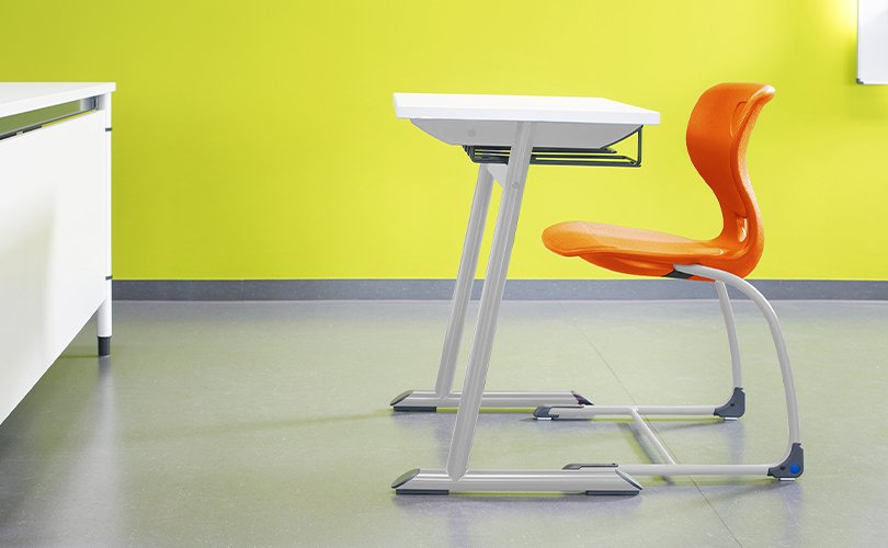 Single student desk with orange chair in classroom