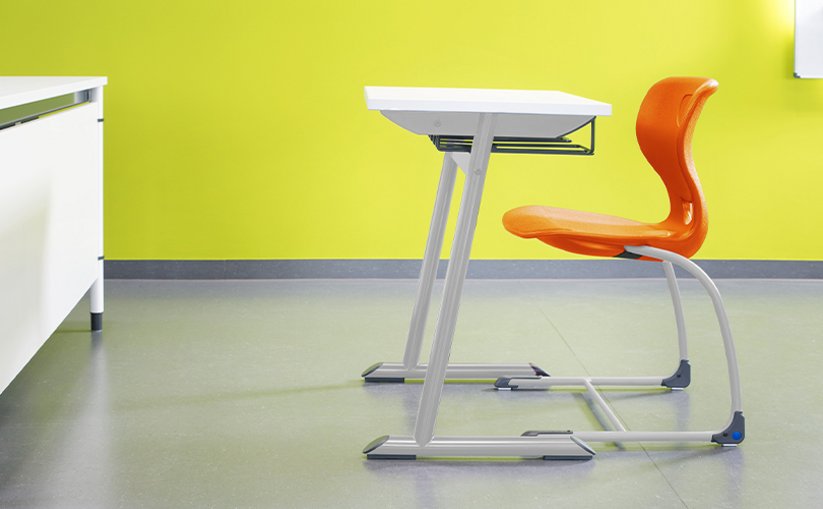 Single student desk with orange chair in classroom