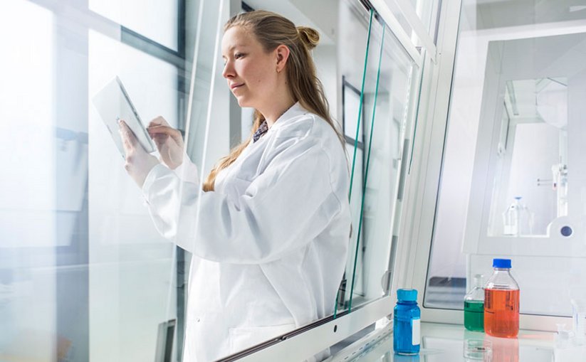 Laboratory worker with tablet in front of fume hood