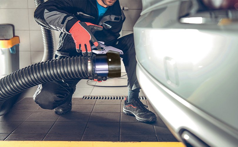 Mechanic connecting a vehicle exhaust extraction hose to a car