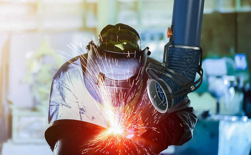 Worker welding metal while an extraction arm captures fumes nearby