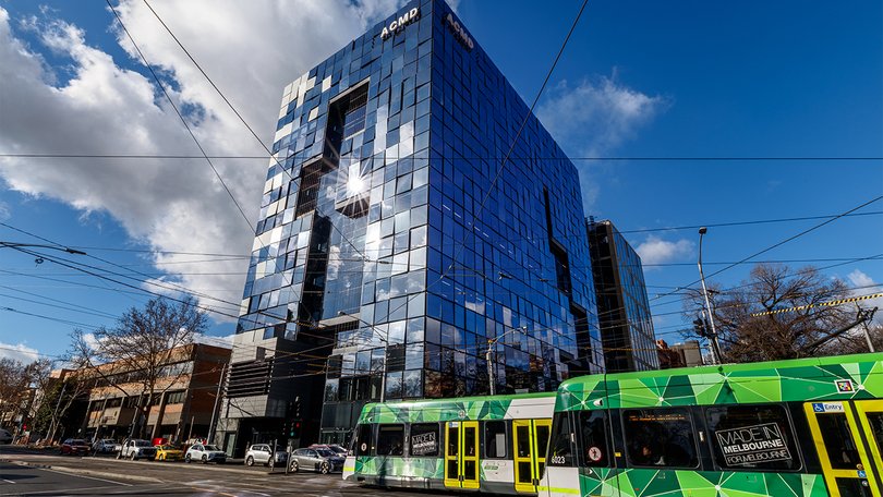 ACMD building exterior with glass façade and tram in front.
