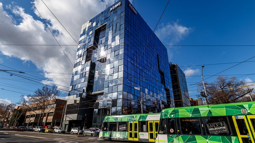 ACMD building exterior with glass façade and tram in front.