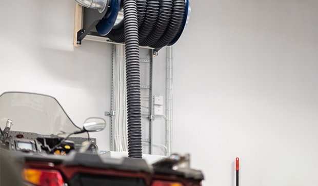 Vehicle exhaust extraction hose mounted on a wall reel, connected with parked vehicle