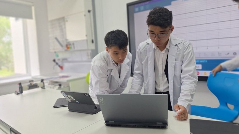 Two students work together on a laptop in a brightly lit laboratory